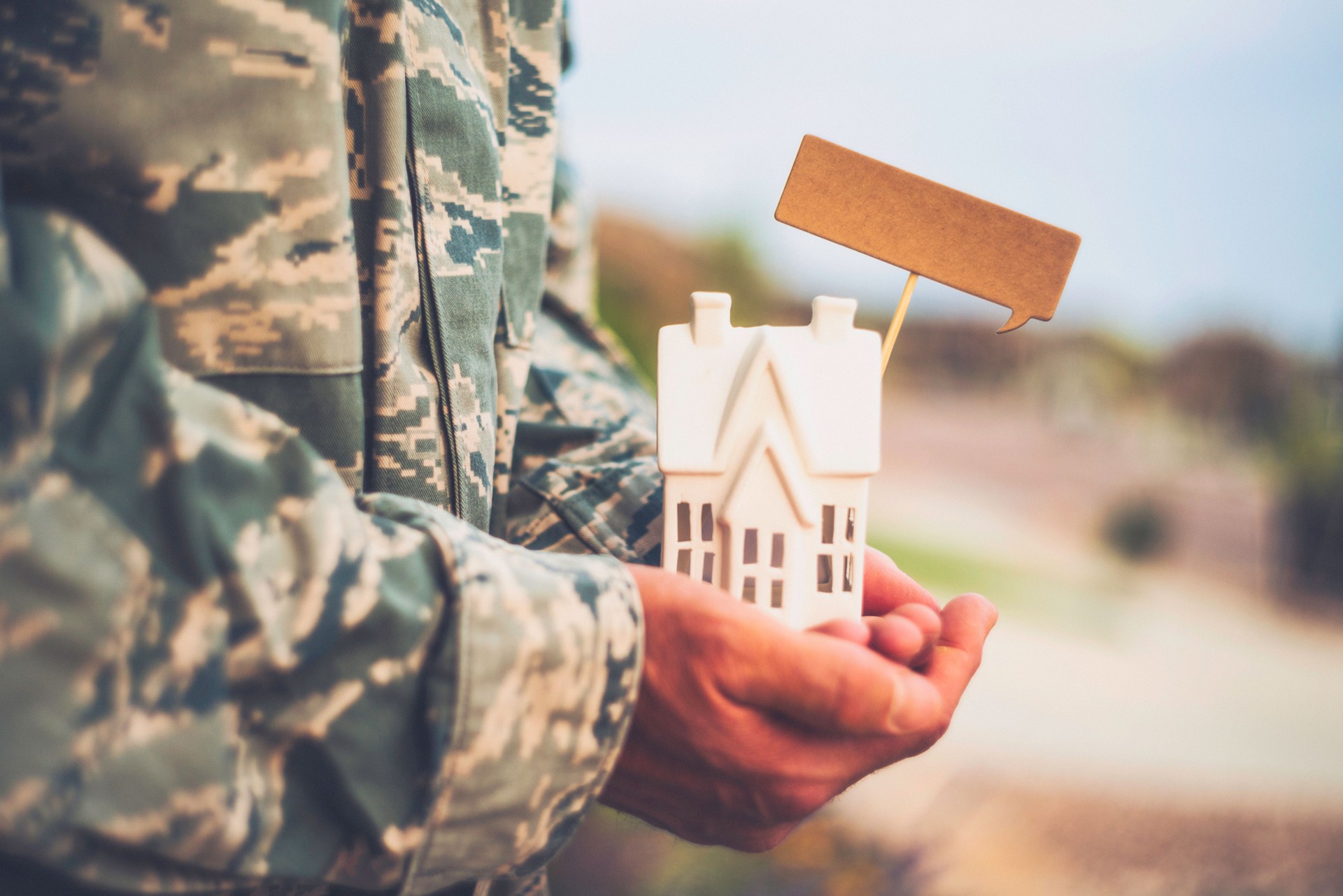 United States Military soldier in uniform holding small house. Relocation concept